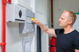 Man Inspecting Fire Alarm System in Workplace
